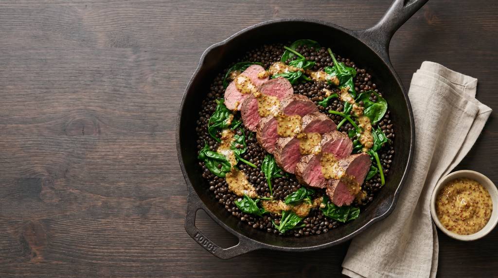 Rinderfilet-Pfanne mit Beluga-Linsen, frischem Spinat und Senf-Dressing in einer gusseisernen Pfanne, von oben fotografiert
