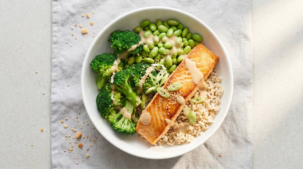 Lachs-Bowl mit gebratenem Lachsfilet, gedämpftem Brokkoli, Edamame, Naturreis und Miso-Dressing in einer weißen Schüssel, bestreut mit Sesam und Frühlingszwiebeln
